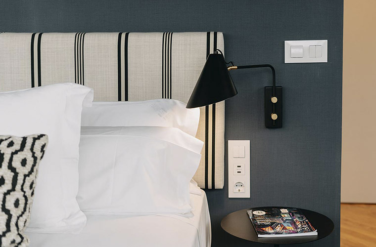 Detalle de una moderna habitación de hotel con elegante cabecero, lámpara de lectura y sábanas blancas impecables para los participantes del Weekend Padel Camp Málaga.