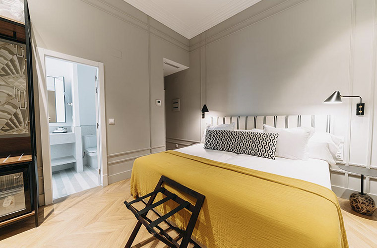 Elegante habitación de hotel con cama king-size, colcha amarilla y baño moderno para los huéspedes del Weekend Padel Camp Málaga.