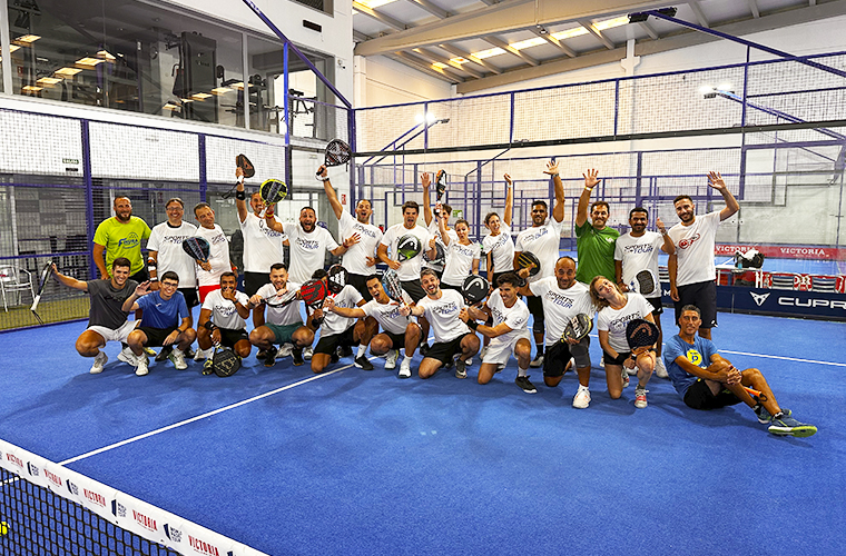 Numeroso grupo de jugadores de pádel en la pista azul celebrando con raquetas y camisetas del Sports Club Tour.