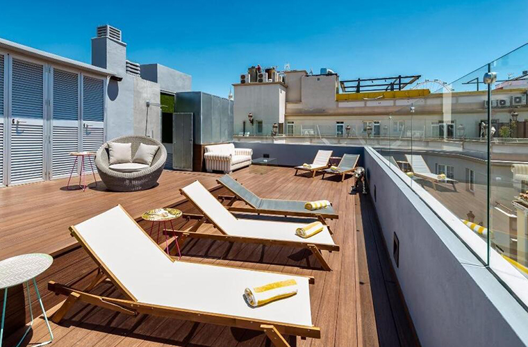 Rooftop sun terrace at Mariposa Hotel Malaga with loungers, seating areas, and city views under a clear blue sky