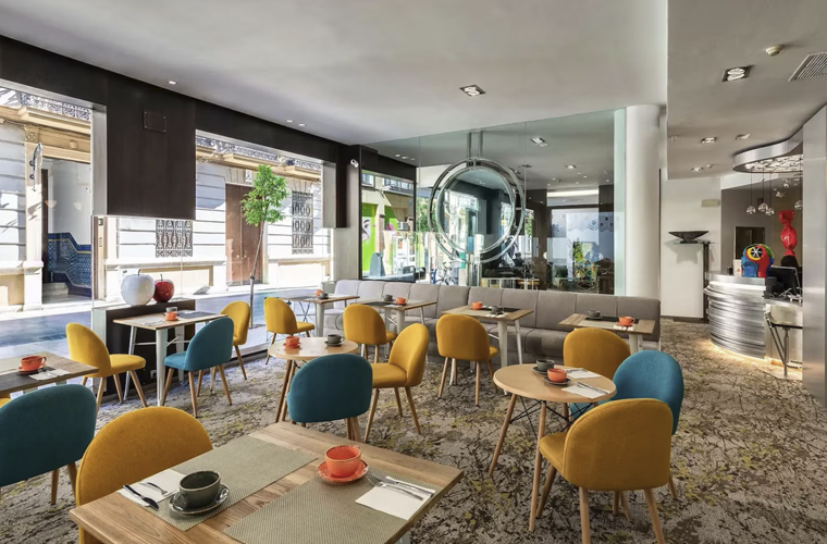 Bright breakfast room at Mariposa Hotel Malaga with colorful chairs and street views, official accommodation for Weekend Padel Camp Malaga