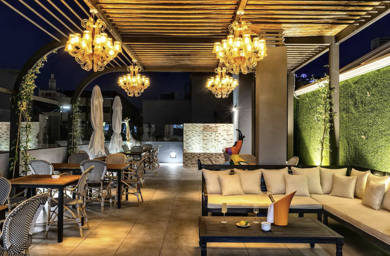 Rooftop lounge at Mariposa Hotel Malaga at night with chandeliers, sofas, and outdoor dining tables