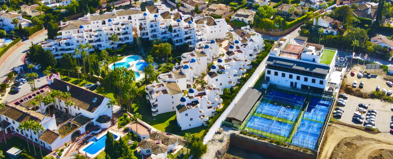 Aerial view of Oxygen Padel Club in Calahonda with multiple blue padel courts next to white residential buildings.